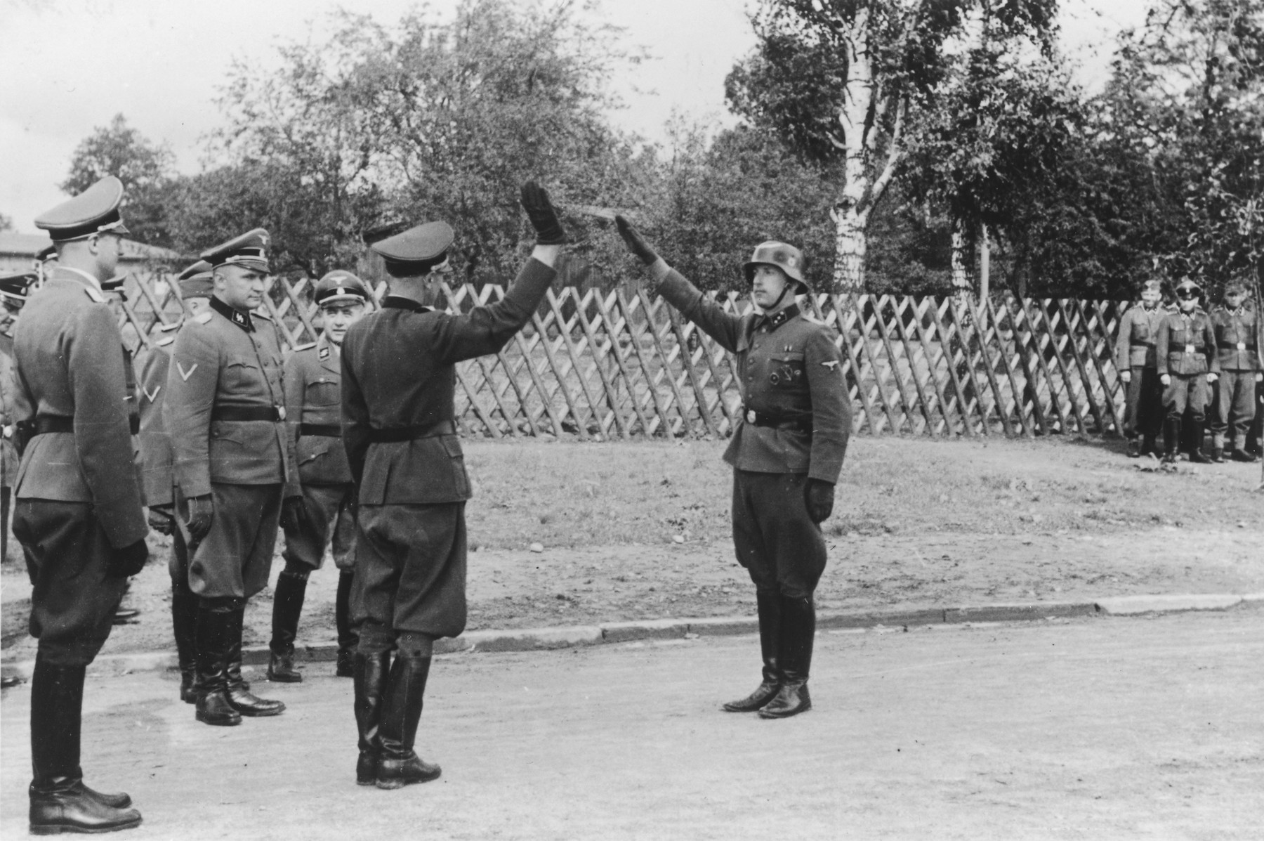 A Nazi soldier salutes an officer, while several other officers stand in the background during the dedication of a new SS hospital in Auschwitz.

The official caption reads "Einweihung des SS-Lazarettes in Auschwitz" (Dedication of the SS Hospital in Auschwitz).

Pictured on the leftt are Dr. Eduard Wirths, Commandant Richard Baer and Karl Bischoff.