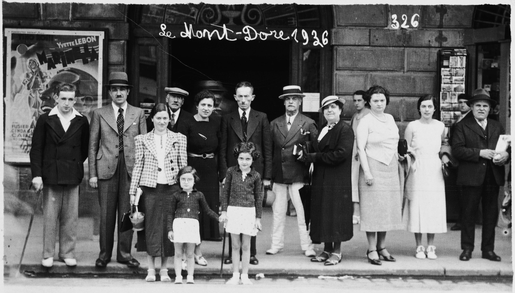 A Jewish family visits Mont-Dore where they pose with a large group in front of a movie poster.

Among those pictured are the Apfel family -- Samuel (second from the left), Fanny, Paulette and Ruth.