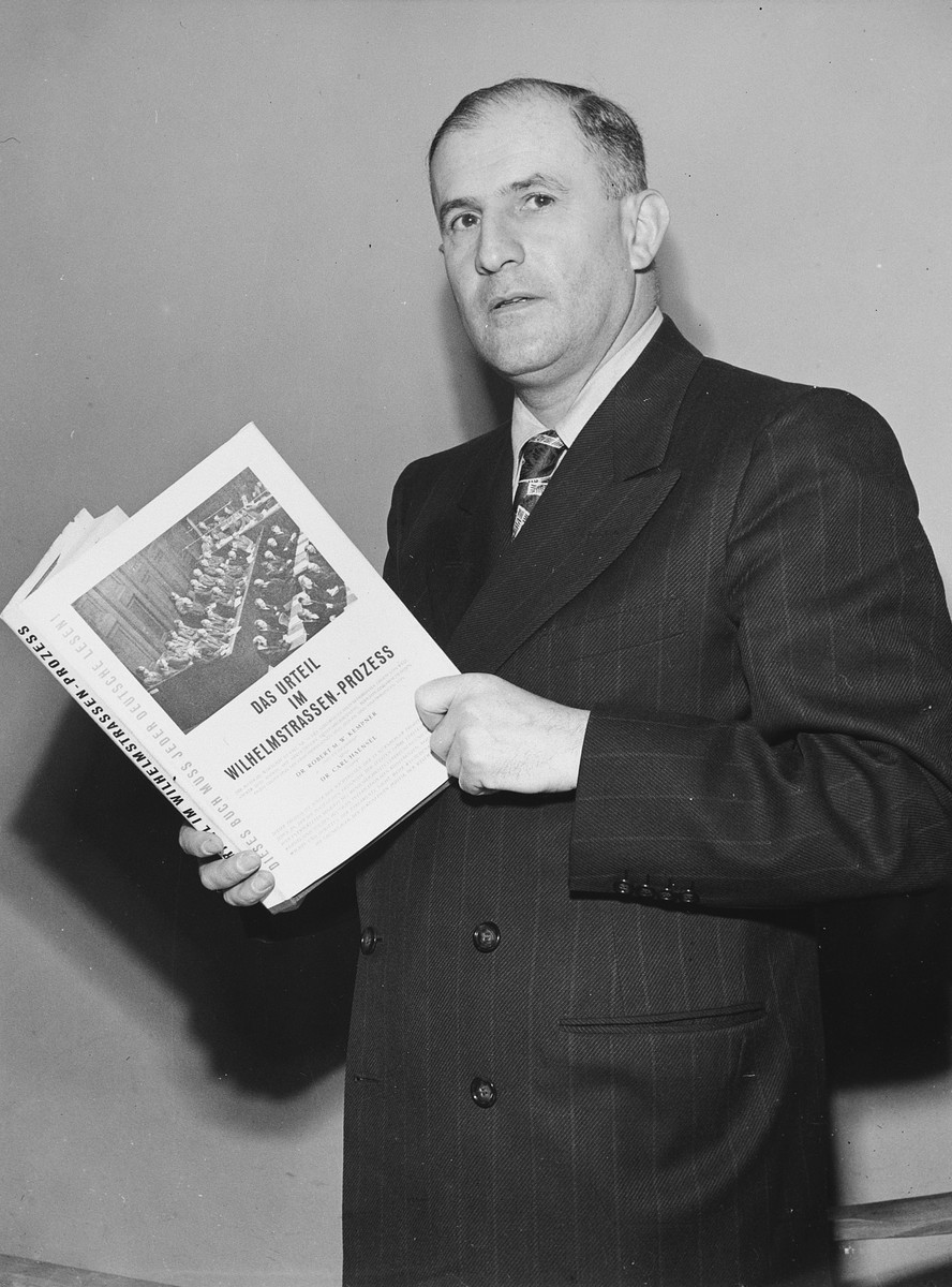 Studio portrait of German-born American attorney, Robert Kempner, holding a book about the Ministries war crime trial which he prosecuted.