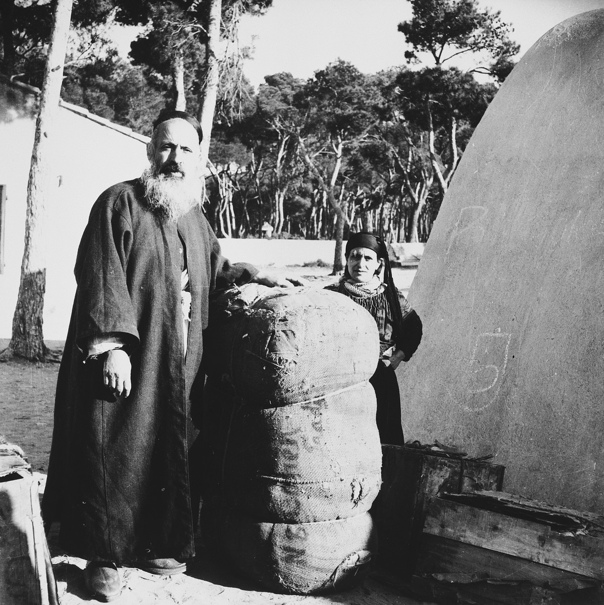 A Morrocan-Jewish man and woman stand next to a large bundle in the Los Arenas camp while waiting to immigrate to Palestine.