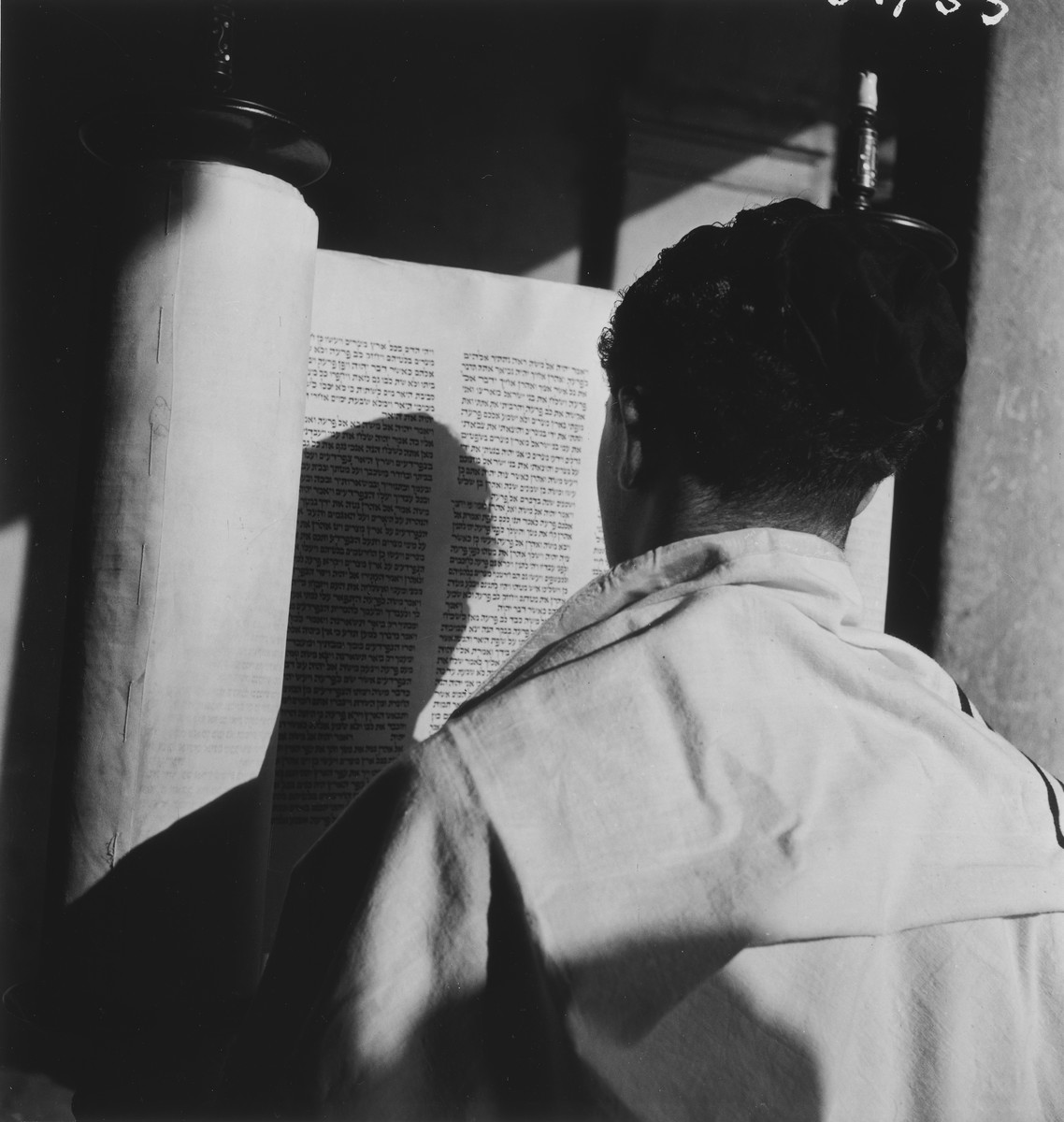 A teenager wrapped in a prayer shawl lifts up the torah scroll during religious services in an unidentified post-war OSE children's home.