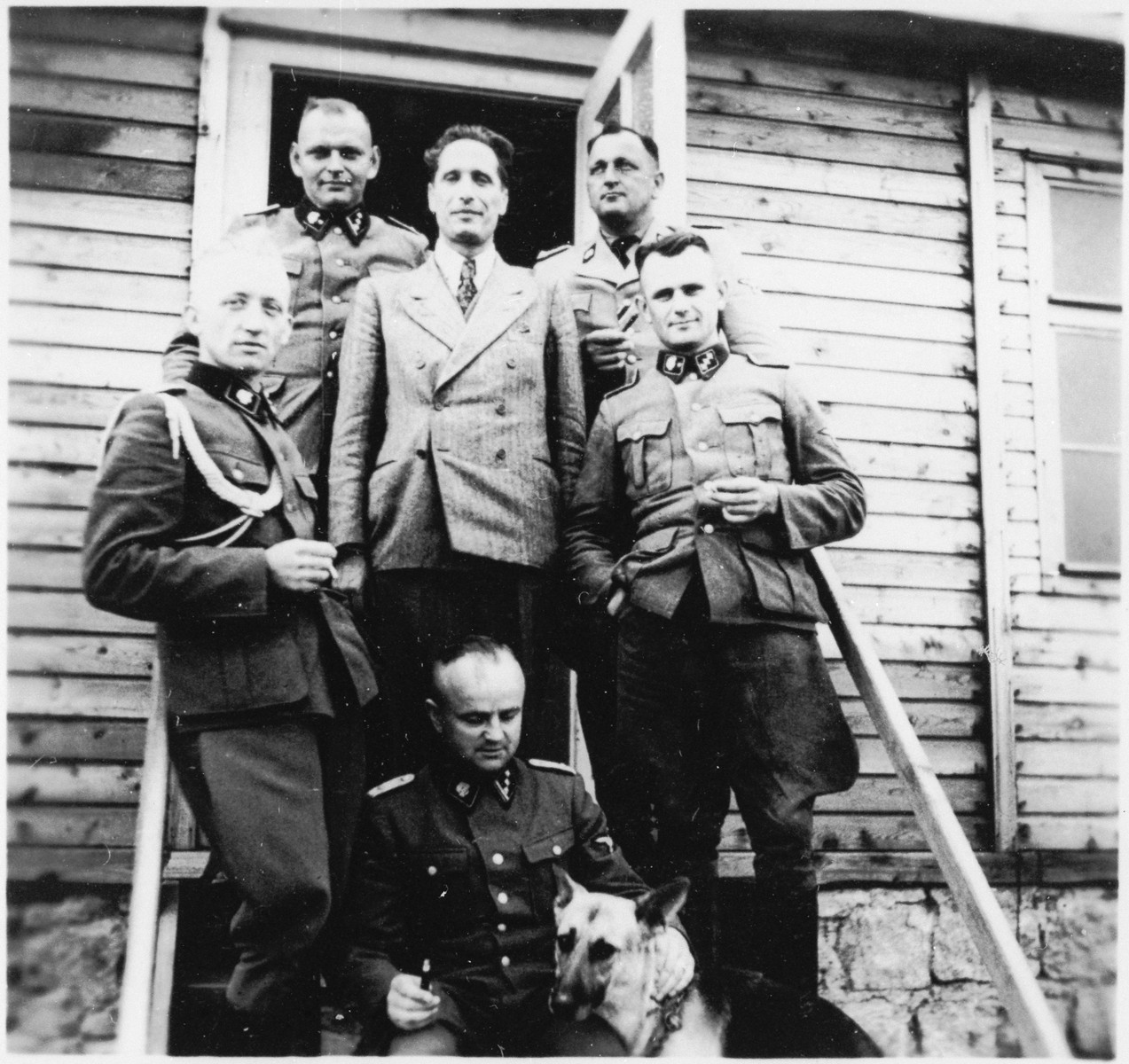 A group of SS officers stand on the steps of a building at the Gross-Rosen concentration camp.

Standing on the far left is the adjutant, Kuno Schramm.  Obersturmfueher Hermann Michl is standing behind him on the top left.  The Commandant Arthur Roedl is on the top right.  Beneath him is including Anton Thumann (bottom right).