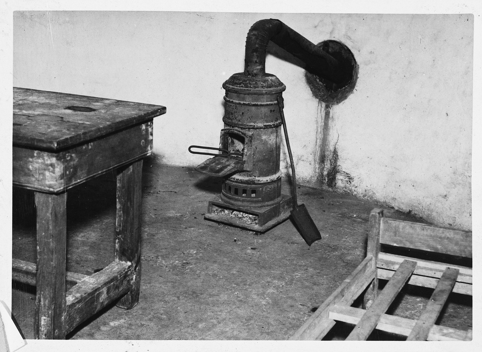 Interior view of a torture chamber in the Breendonck concentration camp.

The original caption reads "Stove, table and bed in the torture chamber.  The prisoners were beaten on the table.  Pokers were heated in the stove."