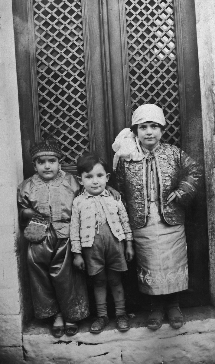 Three young Greek Jewish children pose in front of their home in their Purim costumes.

Pictured in the center is Michael Matsas along with two of his cousins.