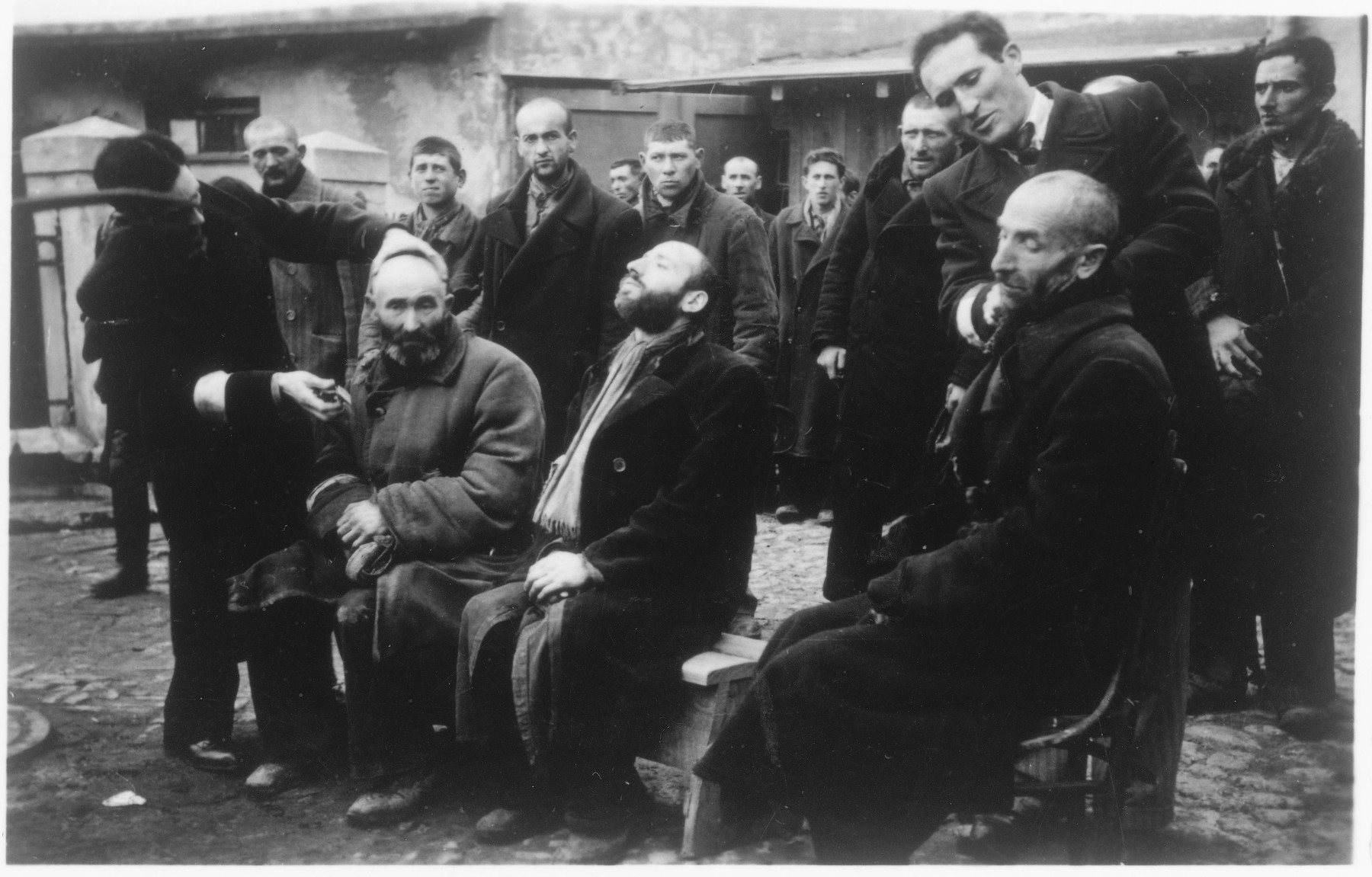 Jewish men are forced to shave the beards of other religious Jews while SS men watch in amusement.

The caption of the SS-Archiv says "Reinrassige Juden bei Schoenheitspflege in Palinin (?) Okt. 1941" (Purebred Jews during beauty care in Palinin (?) Oct. 1941).