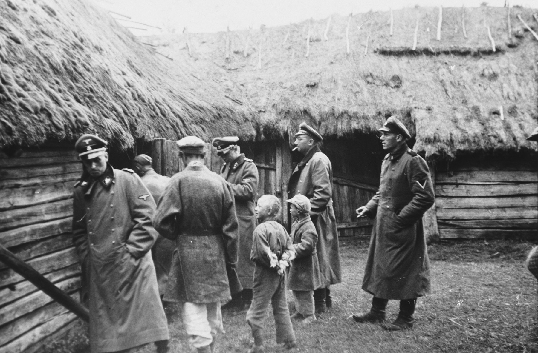 SS officers inspect Russian farmhouses while two children and a civilian look on.

The caption of the SS-Archiv says "Russische Bauernhaeuser in der Prim Okt. 1941" (Russian farmhouses in the Prim October 1941).