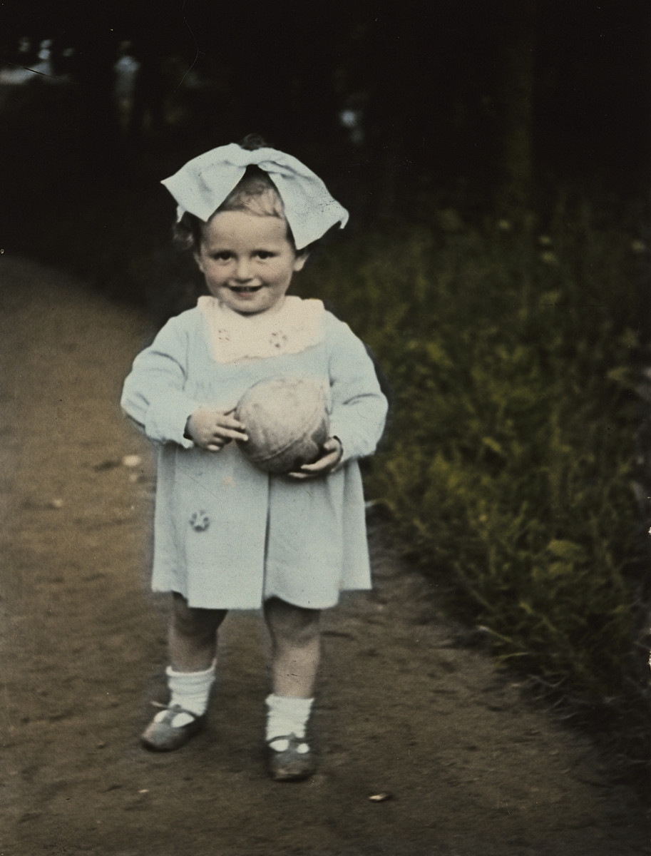 Close-up, colorized portrait of a  young Polish-Jewish toddler with a large bow and a ball.

Pictured is Sala Perec.
