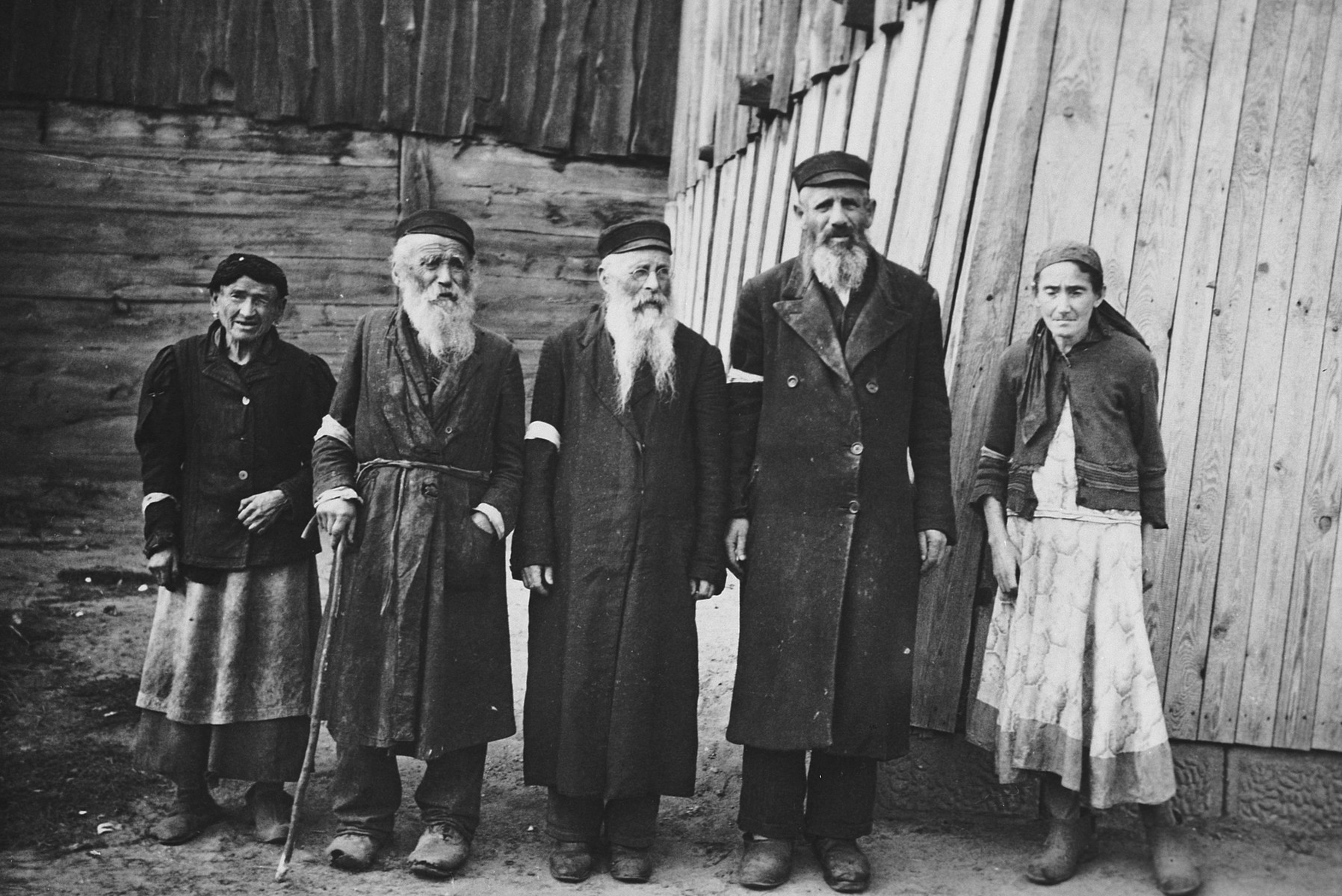 Portrait of two older women and three older men wearing armbands standing in front of a wooden house. 

The caption of the SS-Archiv says "Original Juden in (...) Sept. 1941" (original Jews in (...) Sept. 1941).