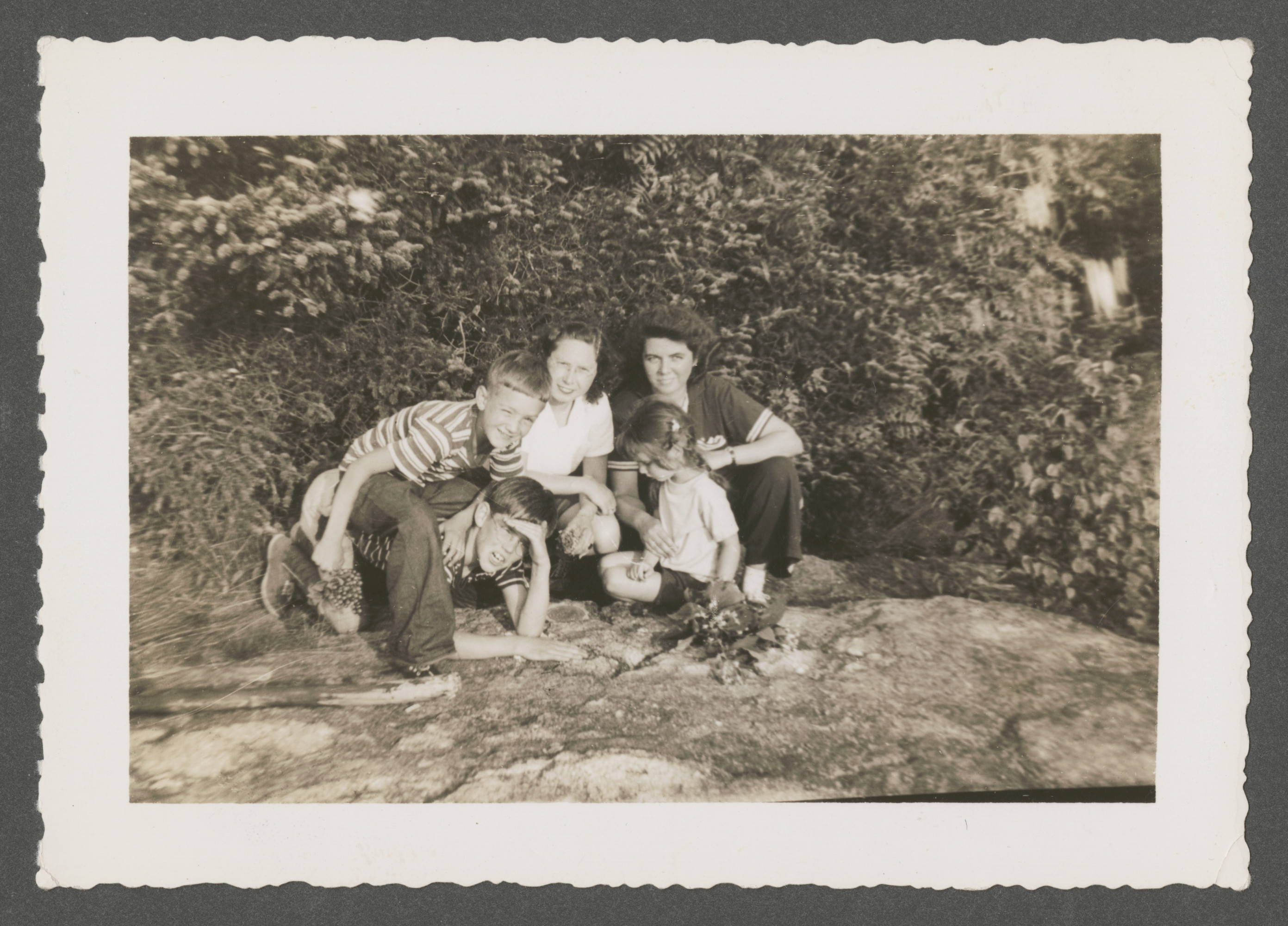 Goldschmied and Sharp family members relax on the peak of Mount Sunapee in New Hampshire.

Pictured is Renee Goldschmied (back, center), with Martha Sharp (back, right) and [probably] her children Hastings (front, on hands and knees) and Martha Content (front, right).  

The inscription on the back of the photograph reads, "Renee on peak of Mount Sunopee, 1214 ft. high, summer 1942 (Sharps)."