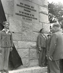 Two survivors wearing their concentration camp uniforms stand at attention in front of the newly dedicated monument to the victims of the Pocking concentration camp.
