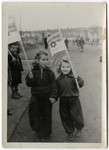 Two young girls walk down a road in the Schlachtensee displaced persons' camp carrying Simchat Torah flags.