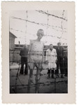 An emaciated, naked survivor stands by the barbed wire fence of the Mauthausen concentration camp after liberation.