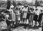 A group of girls stand in a line holding flowers in the Chateau de La Guette children's home.