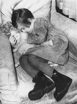 Close-up of a little girl sleeping with her doll in a chair.