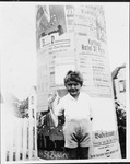 Fritz Glueckstein poses in front of a kiosk covered with announcements and advertisements.