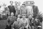 Jewish men, one in concentration camp uniform gather in the Pocking displaced persons camp.