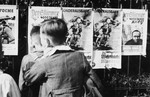 A group of young German boys view "Der Stuermer," "Die Woche," and other propaganda posters that are posted on a fence in Berlin.