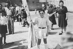 A young Jewish DP child, dressed in the uniform of the Betar Zionist movement, poses with a flag during a ceremony celebrating the establishment of the State of Israel at the Heidenheim displaced persons camp.