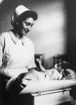 Tonia Rotkopf (now Blair), a nurse at the UNRRA house in the Landsberg DP camp, weighs a newborn baby.