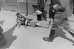 A destitute young man lies on the street in the Warsaw ghetto with a collection cup.