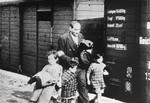 A still from period film footage of a Jewish man walking with three young children alongside a deportation train.