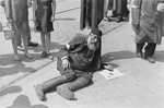 A destitute, elderly man lies on the pavement in the Warsaw ghetto begging for assistance.