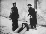 A workman from the Pinkiert funeral home has a man on the street help him pick up a body for burial in the Warsaw ghetto cemetery.
