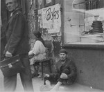 A man begs for change or food while sitting in front of a butcher shop on Nowolipie Street in the Warsaw ghetto.