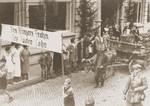 Residents of Altenar view a Thanksgiving Day parade in which two boys carry an anti-Semitic banner that reads, "The vintner's happy harvest is the Jew's payday."  The boys are marching behind an anti-Semitic float depicting a Jew sitting at a counting table, surrounded by enormous bags of money, reveling in his profits from the grape harvest.