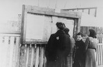 A small group of Jews reads the announcements posted by the Jewish Council in a display box on a street in the Kovno ghetto.