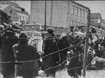 Jews in the Kovno ghetto who have been assembled for deportation, look on while their luggage is loaded onto trucks.