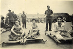Three women sit outside on stretchers in front of an aid workers group and an ambulance