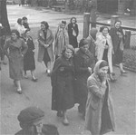 Jewish women wearing yellow stars are walking in the street, near a park.