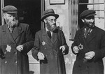 Three Jewish men stand outside a building in the Lodz ghetto.