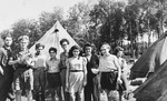 Group portrait of Jewish DP youth standing among a cluster of tents at the Poppendorf displaced persons camp.