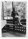 Toby Papier (the donor's aunt) sits on a porch railing overlooking a woods.
