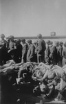Survivors and American soldiers, including a German POW, inspect a pile of corpses in Buchenwald.