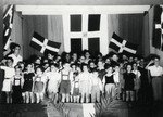 Young children stand in front of Dominican flags at a ceremony in their school in Sosua.