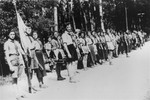 Members of the Hashomer Hatzair Zionist youth movement stand in formation along a road, several of them holding musical instruments.