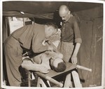 Captain Robert A. Baker of Newberry, S.C., gives medical attention to a former concentration camp prisoner suffering from malnutrition in an airport at Neubau.