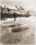 An American soldier walks past the corpse of an American soldier killed by the SS and then run over by a tank during the Malmedy atrocity.