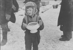 A young boy carrying a bowl of soup, holding food ration tickets.
