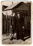 Portrait of a young couple standing by a fence [possibly in the Deblin ghetto].