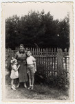 Julius and Bella Menn pose next to the their German governess, Maria Lipke, by a fence in a garden.