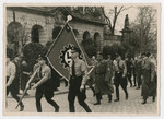 Members off the German Labor Front march down a street in Fulda carrying the Cog Wheel Swastika during a May Day Nazi party parade.