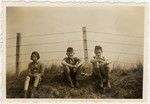 Three children rest during a bike ride to the coast which is blocked off with barbed wire in anticipation of the coming war.