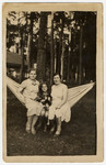 A Lithuanian Jewish woman and her daughter sit together on a hammock with their Lithuanian housekeeper.