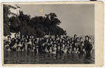 Children in a postwar Jewish summer camp pose for a group portrait in either a lake or the sea.