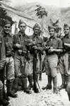 Five Italian soldiers pose with their weapons in a base near a mountain.