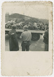 American soldiers watch as the bodies of victims are hauled away on a flat bed truck.